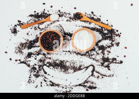 Hausgemachte natürliche Kaffee Körper Peeling, lustige Gesicht mit Holzschalen mit Zutaten und bestreut Produkt mit gemaltem Lächeln auf weißem Tisch, flach legen. Stockfoto