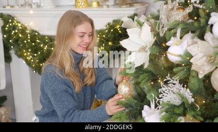 Glückliche junge blonde Frau Dekoration weihnachtsbaum mit Ball an Ihr Zuhause Stockfoto