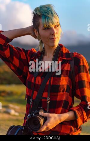 Von oben eine positive Frau, die am Sommertag auf dem karierten Boden liegt und Fotos mit einer altmodischen Kamera auf dem Land fotografiert Stockfoto