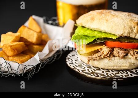 Nahaufnahme von leckeren Schweineburger mit Cheddar-Käse und gebraten Kartoffeln auf dem Tisch in Fast-Food-Café angeordnet Stockfoto