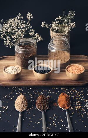 Draufsicht auf verschiedene Körner in Gläsern und aromatischen Gewürzen In Löffeln auf Holztablett auf schwarzem Tisch angeordnet Stockfoto