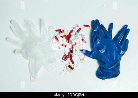 Einige Medikamente auf einem Tisch in der Mitte eines Paares von blauen Handschuhen und .ein weiteres Paar transparente weiße Handschuhe verstreut. Persönliche Schutzausrüstung- Stockfoto