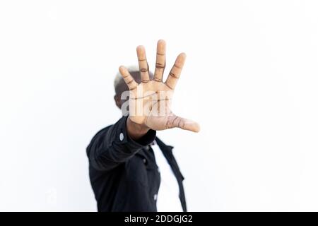 Anonymer afroamerikanischer Rüde im lässigen Outfit, der Hand entgegen reicht Kamera und Deckblatt beim Stehen auf der Straße und beim Vorführen Geste anhalten Stockfoto