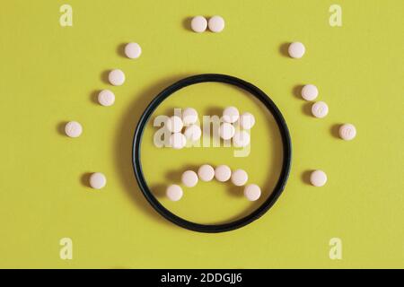 Ein trauriges Smiley-Gesicht, bestehend aus Pillen in einem kreisförmigen Filter mit Medikamenten auf einem leuchtend gelben Hintergrund. Stockfoto