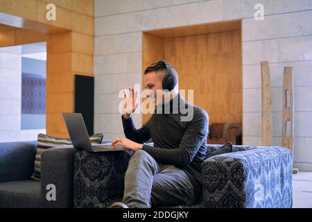 Entzückte junge Mann in Kopfhörer winkende Hand, während mit Video Rufen Sie über Netbook und lächeln Stockfoto