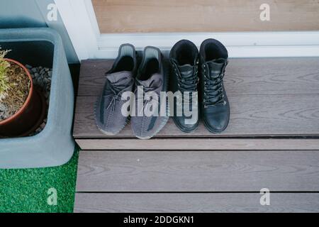 Von oben von männlichen Sneakers und weiblichen Lederstiefeln platziert Auf hölzerner Stufe am Eingang der Kabine Stockfoto