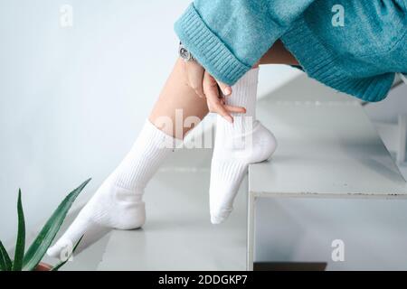 Seitenansicht der anonymen Frau in weißen Socken und warm Pullover auf der Treppe im hellen Haus sitzen Stockfoto