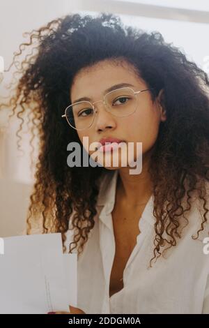 Bestimmte afroamerikanische weibliche Unternehmer sitzen in hellen Büro mit Dokumente und Blick auf die Kamera Stockfoto