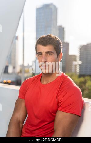 Junge muskulöse männliche in Sportbekleidung Ruhe nach intensivem Training auf Terrasse des modernen Stadtgebäudes mit Blick auf die Kamera Stockfoto