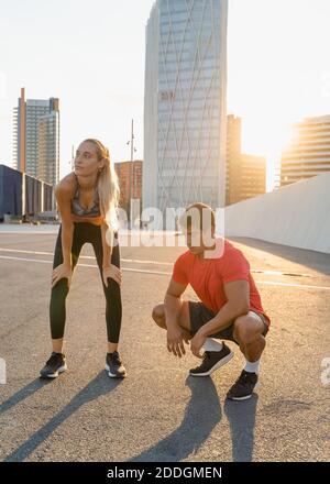 Ein paar Athleten in Sportbekleidung, die auf Asphalt hinter sich liegen Stadtgebäude nach dem Training im Hinterlicht Stockfoto