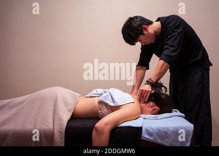 Seitenansicht der jungen asiatischen Patientin, die vor Schmerzen weint Während der professionellen osteopathischen Massage von Therapeuten in der Klinik Stockfoto