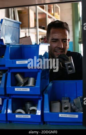 Positive Erwachsene männliche Meister in Schutzhandschuhen Kommissionierung Metall Detail Von Box bei der Auswahl von Werkzeugen für Reparaturservice in der Werkstatt Stockfoto