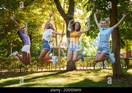 Volle Länge optimistisch aktive Teenager weibliche Freunde springen hoch mit Arme angehoben, während Spaß zusammen im Sommerpark Stockfoto