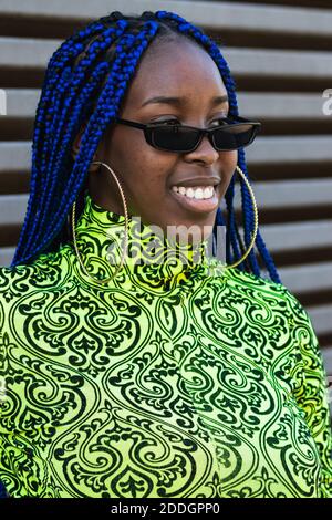 Selbstbewusst glücklich afroamerikanische Frau mit blauen Zöpfen tragen trendy Outfit und Sonnenbrille stehen auf der Straße und schauen weg Stockfoto