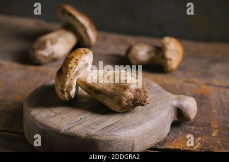 Zusammensetzung von rohen ganzen Steinpilzen oder cep Pilze beim Schneiden Brett in Holz rustikalen Tisch Stockfoto