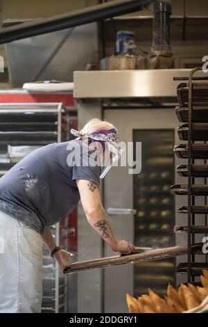Seitenansicht der Arbeiterin in Maske und Schildherstellung Kerben auf Laibe des Baguette-Teigs beim Zubereiten des Teigs Backen Stockfoto