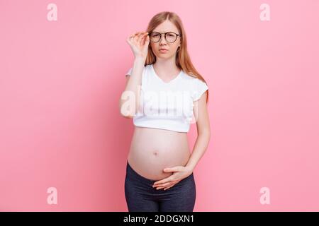Schwangeres Mädchen in einem T-Shirt mit Brille für Sehbehinderte. Auf rosa Hintergrund, Vision Loss Konzept. Stockfoto