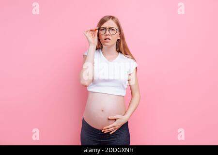 Schwangeres Mädchen in einem T-Shirt mit Brille für Sehbehinderte. Auf rosa Hintergrund, Vision Loss Konzept. Stockfoto
