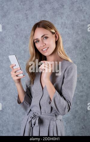 Aufnahme einer jungen Geschäftsfrau, die ein Mobiltelefon benutzt, während sie die Kamera anschaut und lächelt. Stockfoto