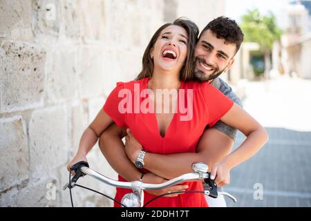 Aufnahme eines glücklichen jungen Paares, das durch ein Fahrrad fährt Die Stadt Stockfoto