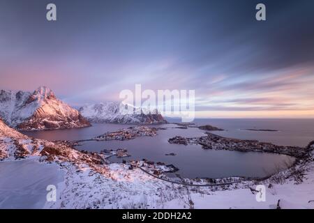 Fantastischer violetter Sonnenaufgang vom Reinebringen-Gipfel aus gesehen. Blick auf Reinevatnet See, reine Dorf und Fjord im verschneiten Winter. Lofoten, Norwegen Stockfoto