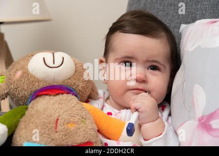 Kranke Mädchen mit Thermometer im Mund für die Messung Körper Temperatur hält bunte Teddybär Spielzeug mit kalten Grippe-Symptome Als pandemische Familie t Stockfoto