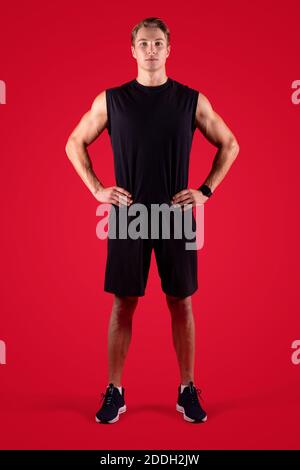 In voller Länge Porträt von bestimmten männlichen Fitness-Modell Blick auf Kamera auf rotem Studiohintergrund Stockfoto