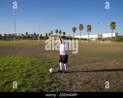 Ein Fußballspieler mit einem weißen Hemd, das sein Gesicht bedeckt Vor dem Sonnenlicht in einem Fußballfeld Stockfoto