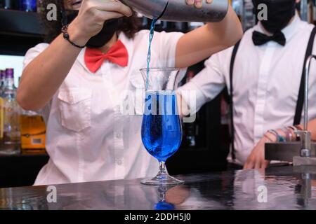 Nicht erkennbare Kellnerin trägt eine schützende Gesichtsmaske und bereitet Cocktails in einem Pub zu. Neue Normalität in Pubs. Stockfoto