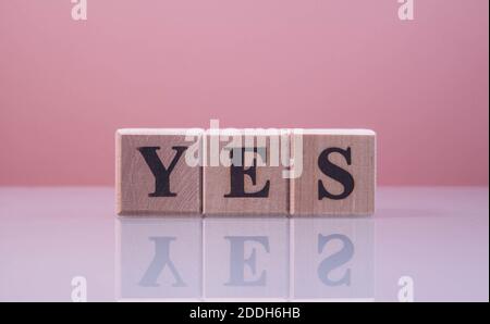 Text JA auf Holzwürfelblöcken. Die Buchstaben JA auf den Würfeln in schwarzen Buchstaben auf einer Glasoberfläche isoliert geschrieben. JA Text für Ihr Design. Stockfoto