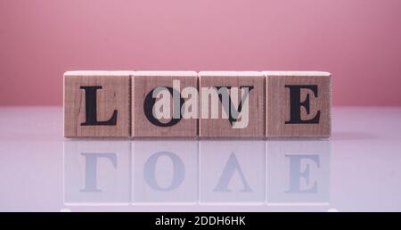 Text LIEBE auf Holz Würfel Blöcke. Die Buchstaben LIEBE auf den Würfeln in schwarzen Buchstaben isoliert auf einer Glasoberfläche geschrieben. LIEBE Text für Ihr Design. Stockfoto
