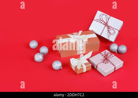 Vier schimmernde Geschenkschachteln mit silbernen weihnachtskugeln auf hellrotem Hintergrund. Konzept zur Feier des neuen Jahres. Geschenke für die Liebsten auswählen Stockfoto