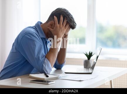 Gestresste männliche Freiberufler sitzen am Schreibtisch im Home Office, mit geschäftlichen Problemen Stockfoto
