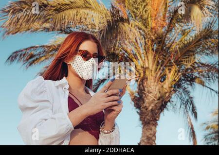 Frau trägt Gesichtsmaske mit Telefon im Freien. Reisekonzept. Stockfoto
