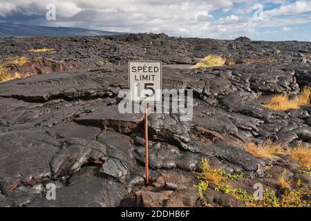 Erstarrte Lava fließen über das Land und die Ostküstenstraße mit einem Geschwindigkeitsbegrenzungszeichen halb bedeckt, auf Hawaii Island, Hawaii Stockfoto