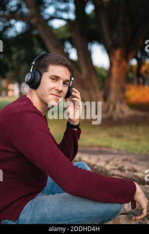 Blonde junge Musik auf kabellosen Kopfhörern auf dem Boden sitzend in die Kamera zu hören. Genießen Sie das Lied. Musikalisches Konzept. Roter Pullover. Stockfoto