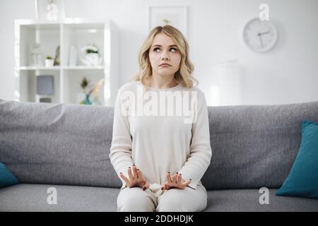 Verwirrt Frau sitzt auf grauen Couch Stockfoto