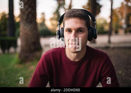 Blonde junge Musik auf kabellosen Kopfhörern auf dem Boden sitzend in die Kamera zu hören. Genießen Sie das Lied. Musikalisches Konzept. Roter Pullover. Stockfoto