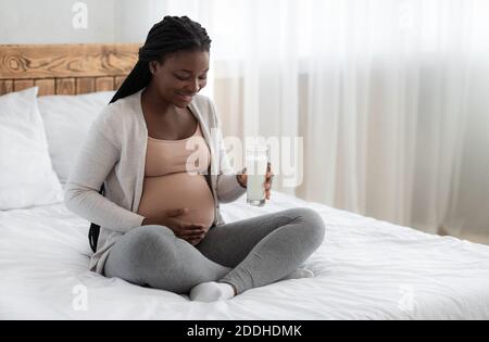 Kalzium Während Der Schwangerschaft. Schwarz Schwangere Frau Sitzt Auf Bett Holding Milchglas Stockfoto