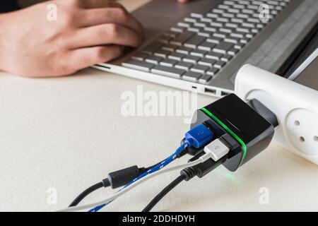 Eine Nahaufnahme verschiedener Kabel, die an mehrere USB-Anschlüsse angeschlossen sind Ladegeräte auf einem Laptop auf einem Schreibtisch Stockfoto