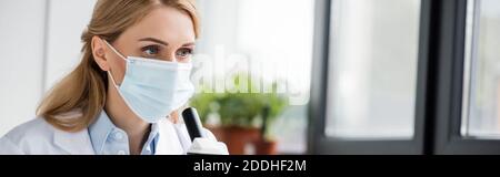 Wissenschaftlerin in medizinischer Maske schaut im Labor weg, Banner Stockfoto