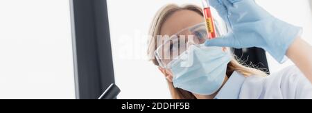 Wissenschaftler in medizinischen Maske und Brille hält Reagenzglas mit covid Schriftzug, Banner Stockfoto