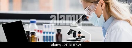 Wissenschaftler in medizinischen Maske und Brille durch Mikroskop, Banner Stockfoto