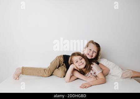 Fröhliche Geschwister liegen in entgegengesetzter Richtung auf einem Tisch. Junge umarmt Mädchen Stockfoto