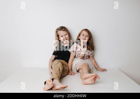 Frech Junge umarmt Mädchen, lehnt sie sich weg. Geschwister sitzen zusammen auf einem Tisch. Stockfoto