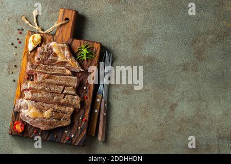 Nahaufnahme fertig zum Essen Steak Ribeye Rassen von schwarzen Angus mit Kräutern, Knoblauch und Butter auf einem Holzbrett. Das fertige Gericht zum Abendessen auf einem dunklen Stein Stockfoto