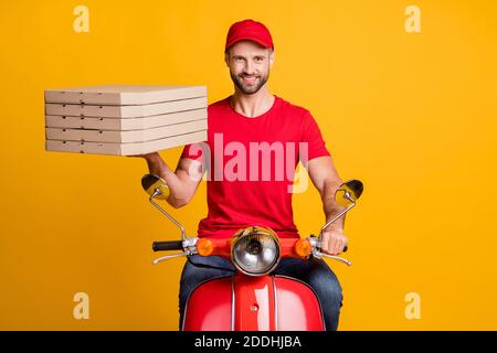 Foto der Lieferung Kerl Kurierfahrt Moped halten Haufen Pizza Boxen tragen rote T-Shirt Kappe isoliert gelbe Farbe Hintergrund Stockfoto