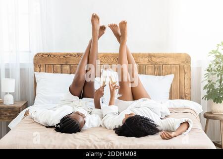 Sorgenfreie afroamerikanische Damen liegen auf dem Bett mit den Beinen nach oben Stockfoto