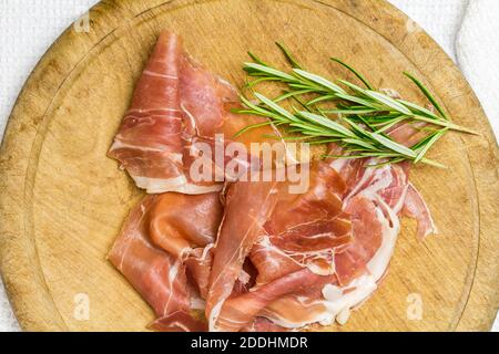 Crudo Schinken mit Rosmarinzweigen auf rustikalem Holzbrett - Draufsicht des Prosciutto Stockfoto