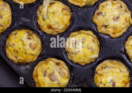 Mini-Quiches mit Speck, Ei, Käse und Petersilie in Backform - herzhafte Törtchen Draufsicht Stockfoto